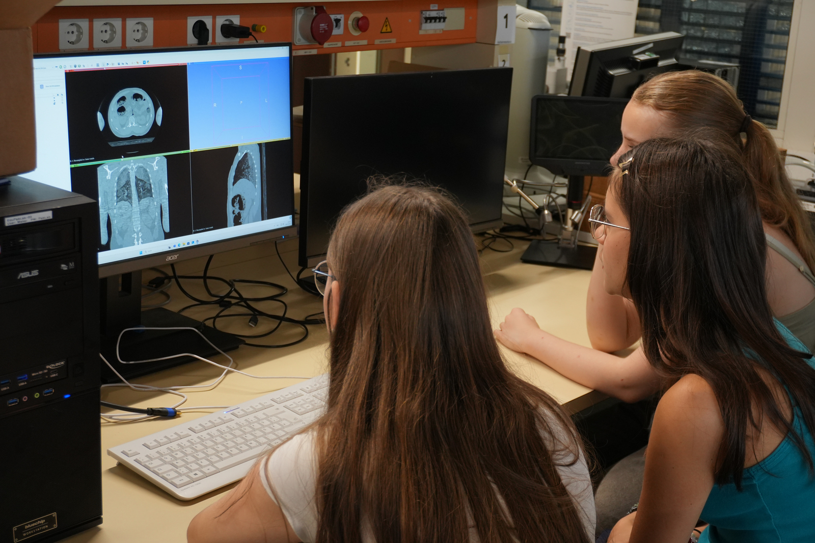 Drei Mädchen sitzen vor einem Computer auf dem Schichtaufnahmen von einem Schädel und einem Oberkörper zu sehen sind