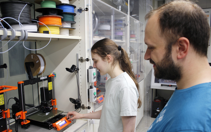 Ein Mädchen und ein Mann stehen an einem 3D-Drucker