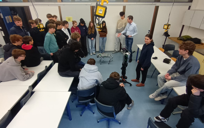 Schüler*innen stehen in einem Klassenraum um einen humanoiden Roboter und einen Roboter-Hund herum